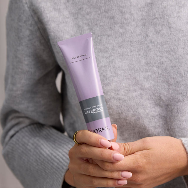 Model applying WØRKS Bergamot Hand Cream from 80ml aluminium tube — a bright, citrus blend of bergamot, petitgrain, and cedar.