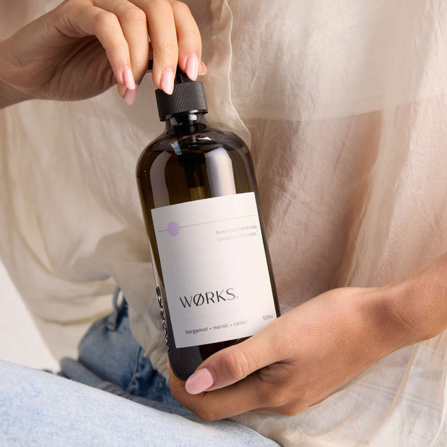 Model using WØRKS Bergamot Hand Soap in 500ml smoky glass bottle — a vibrant blend of bergamot, petitgrain, and cedar.