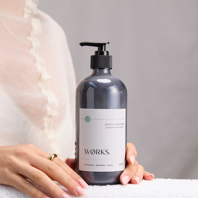 Model moisturising with WØRKS Cumquat Hand Cream in 500ml smoky glass bottle — fresh notes of cumquat, jasmine, and moss.
