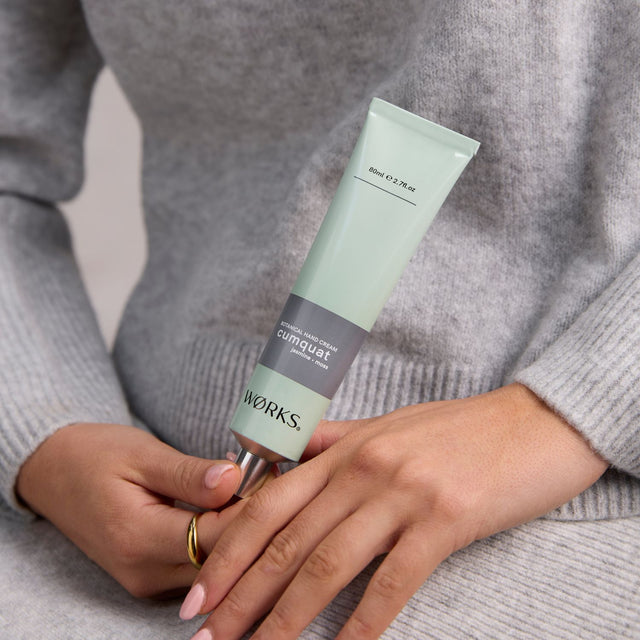 Model using WØRKS Cumquat Hand Cream in 80ml aluminium tube — a fresh, green blend of cumquat, jasmine, and moss.