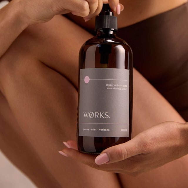 Model lathering WØRKS Peony Body Soap in 500ml glass bottle — fresh notes of peony, mint, and verbena.