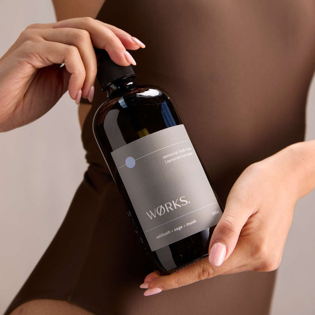 Model bathing with WØRKS Saltbush Body Soap in 500ml smoky glass bottle — grounding blend of saltbush, sage, and musk.