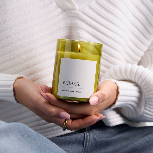 Model lighting WØRKS Saltbush Candle in green glass vessel — a calming blend of saltbush, sage, and musk.