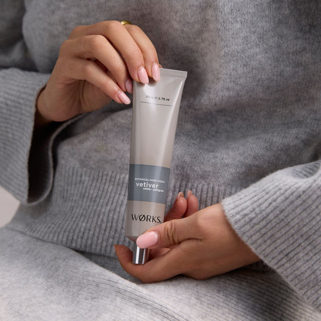 Model smoothing on WØRKS Vetiver Hand Cream from 80ml aluminium tube — a grounding blend of vetiver, nettle, and petitgrain.