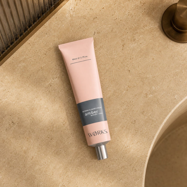 WØRKS Amber Botanical Hand Cream 80ml tube styled in situ on a bathroom shelf