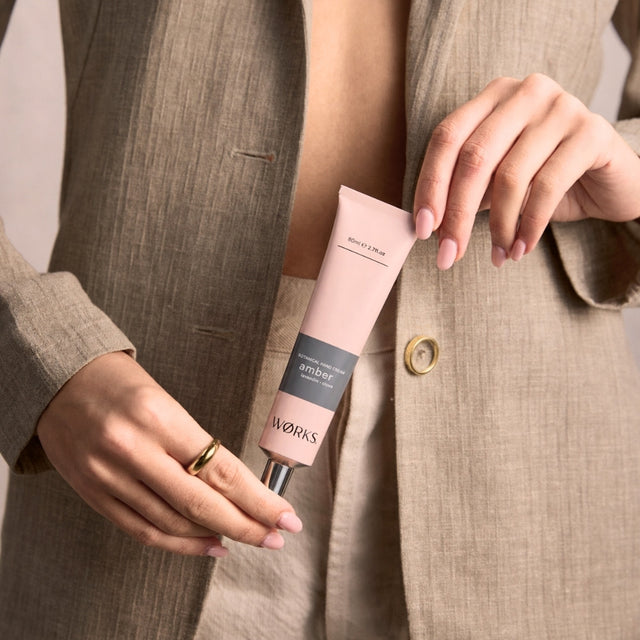 Model holding WØRKS Amber Botanical Hand Cream in an 80ml plastic-free aluminium tube