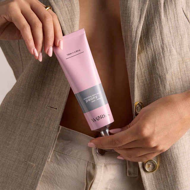 Model applying WØRKS Peony Body Balm from a 120ml aluminium tube — a fresh, textural blend of peony, mint, and verbena.