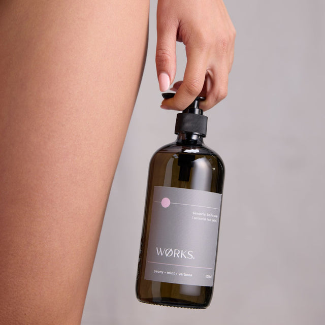 A model in the shower holding WØRKS Peony Body Soap, highlighting a clean, minimal bathing ritual.

