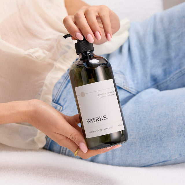 Model using WØRKS Vetiver Hand Soap in 500ml smoky glass bottle — a rich, grounding blend of vetiver, nettle, and petitgrain.